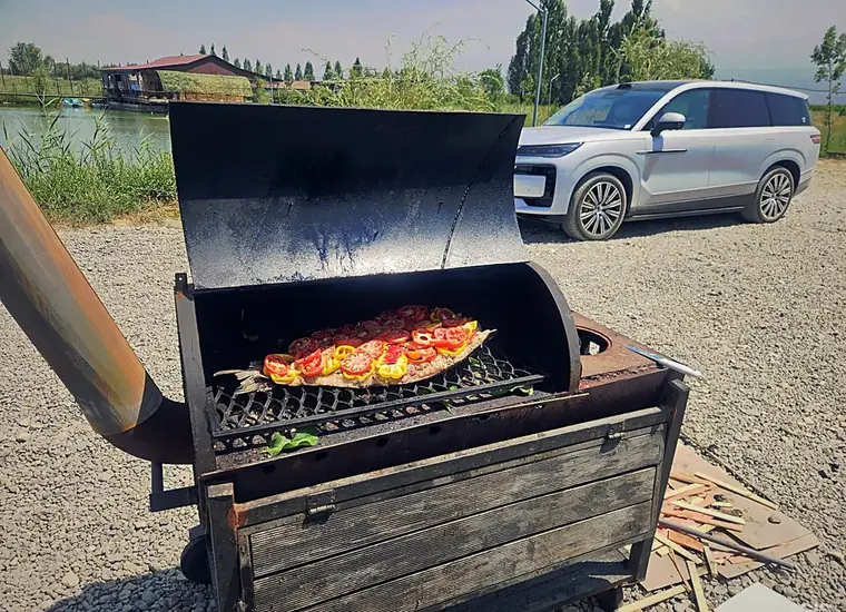 Большой мангал с рыбой и овощами на решётке, рядом озеро